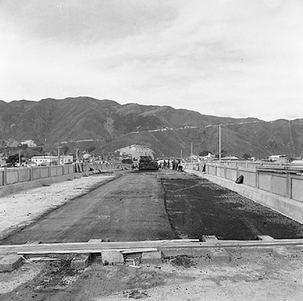 a. Construction of new bridge, workmen, machinery, motor vehicles. Road is being resurfaced