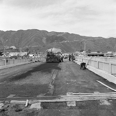 b. Construction of new bridge, workmen, machinery, motor vehicles. Road is being resurfaced