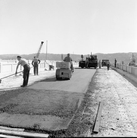 d. Construction of new bridge, workmen, machinery, motor vehicles. Road is being resurfaced