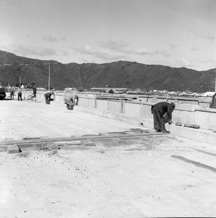 f. Construction of new bridge, workmen, machinery, motor vehicles. Road is being resurfaced