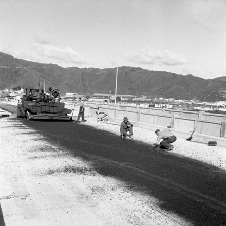 g. Construction of new bridge, workmen, machinery, motor vehicles. Road is being resurfaced