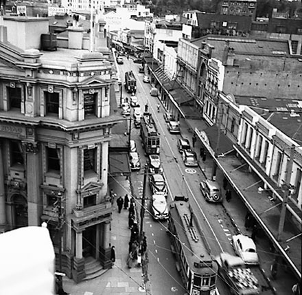 c. Elevated view of Manners Street from James Smith Corner. Bank of New Zealand on corner of Cuba Street. Motor vehicles and tramcars