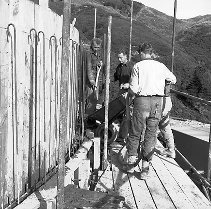 a. View of construction site, workmen are pouring concrete into framing