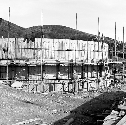 b. View of construction site, workmen are pouring concrete into framing
