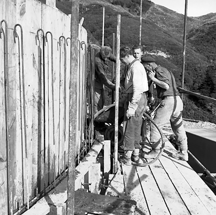 d. View of construction site, workmen are pouring concrete into framing