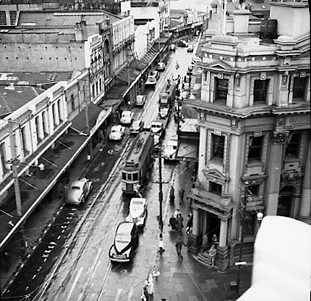 c. Elevated view of Manners Street from James Smith Corner. Bank of New Zealand on corner of Cuba Street. Motor vehicles and tramcars