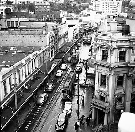 d. Elevated view of Manners Street from James Smith Corner. Bank of New Zealand on corner of Cuba Street. Motor vehicles and tramcars