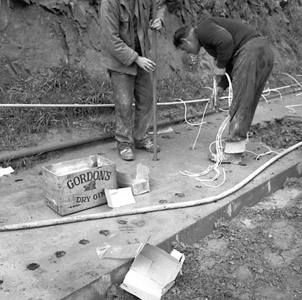 j. Possibly explosives being used to demolish a portion of the hillside. Workmen are preparing site. Elevated view of site with large cloud of dust