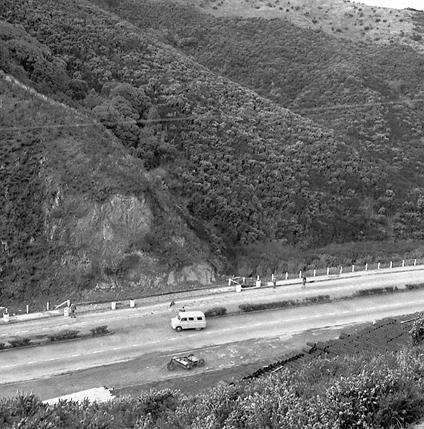 k. Possibly explosives being used to demolish a portion of the hillside. Workmen are preparing site. Elevated view of site with large cloud of dust