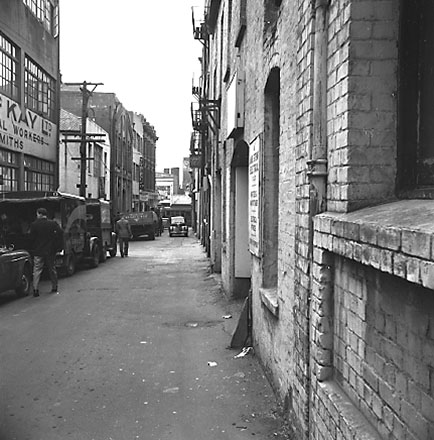 b. Motor vehicles / trucks parked in Herbert Street, commercial buildings. C R McKay, Sheet Metal Workers on the left on the corner of Edward Steet. Looking north towards Manners Street. Herbert Street became part of Victoria Street when Victoria Street w