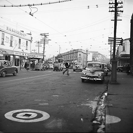e. John Street and Riddiford Street intersection, pedestrians, tramcars, motor vehicles, retail buildings