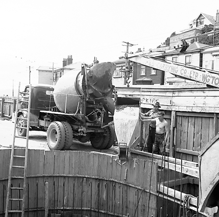 b. Workmen using a concrete mixer truck to pour concrete, truck crane in background