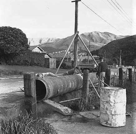 f. Large concrete pipe being laid in a trench. Workmen are using a digger to dig the trench and transfer the pipe from the back of a truck. Contractor is C R Quinn