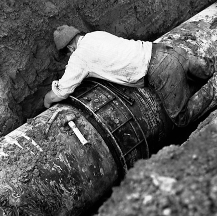 g. Large concrete pipe being laid in a trench. Workmen are using a digger to dig the trench and transfer the pipe from the back of a truck. Contractor is C R Quinn