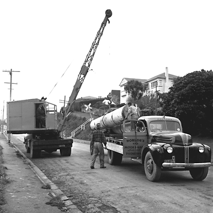 h. Large concrete pipe being laid in a trench. Workmen are using a digger to dig the trench and transfer the pipe from the back of a truck. Contractor is C R Quinn