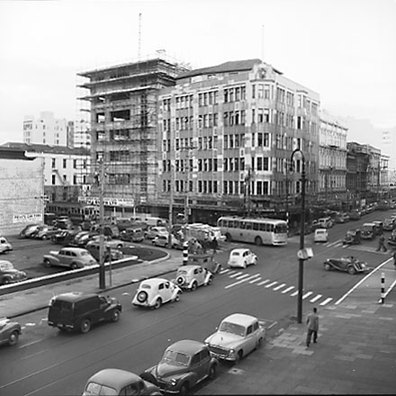 f. Elevated view of intersection, from roof of Town Hall Portico. Civic Chambers building (25-31 Cuba Street, 132-136 Wakefield Street) on the opposite corner, next to Anvil House (138-140 Wakefield Street) under construction. Motor vehicles, trolley bus,