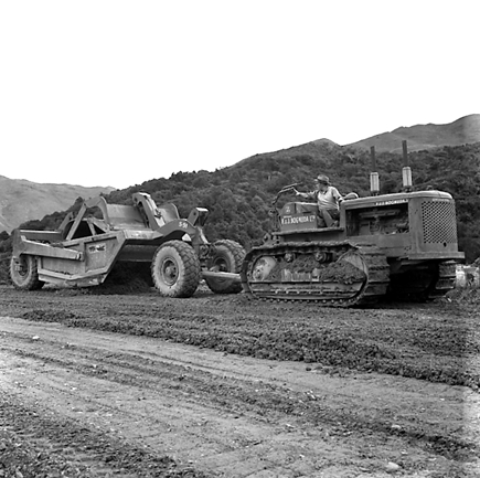 c. views of construction work in progress, workmen, equipment, graders, front end loaders, trucks, dwellings in the background