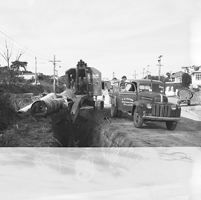 g. views of construction work in progress, workmen, equipment, graders, front end loaders, trucks, dwellings in the background