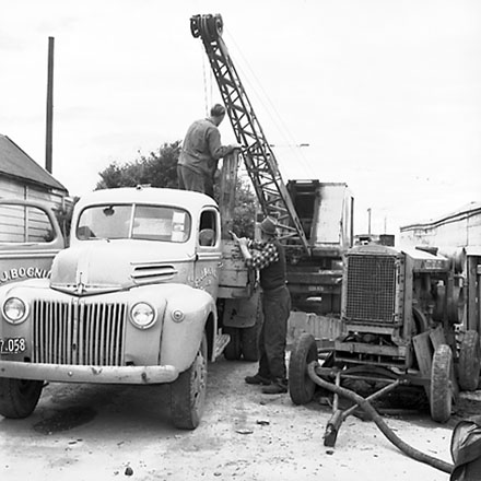 b. Workmen using crane truck to manoeuvre building materials into pumping station, interior of pumping station