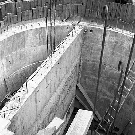c. Workmen using crane truck to manoeuvre building materials into pumping station, interior of pumping station