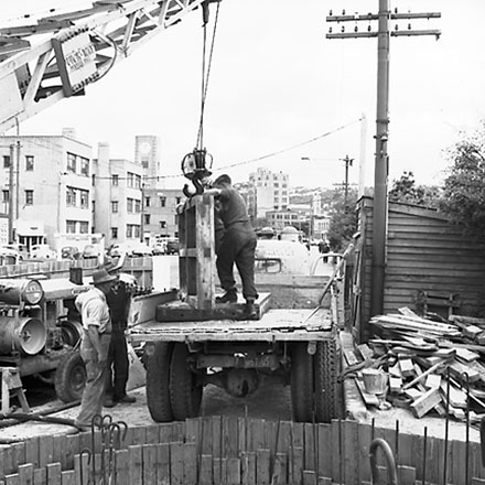 d. Workmen using crane truck to manoeuvre building materials into pumping station, interior of pumping station