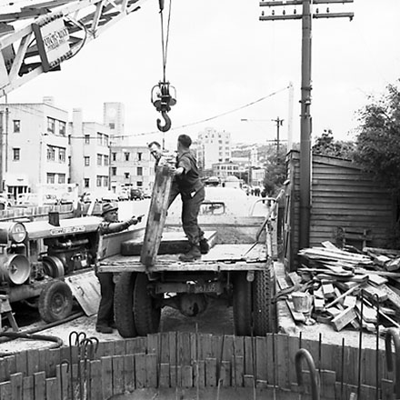 a. Workmen using crane truck to manoeuvre building materials into pumping station, interior of pumping station