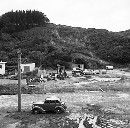 a. Workmen are pouring concrete, from concrete mixer into pipe leading into underground chamber