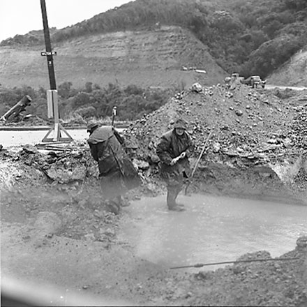 a. Workmen in wet weather clothing are repairing drains - possibly has been a burst or broken pipe
