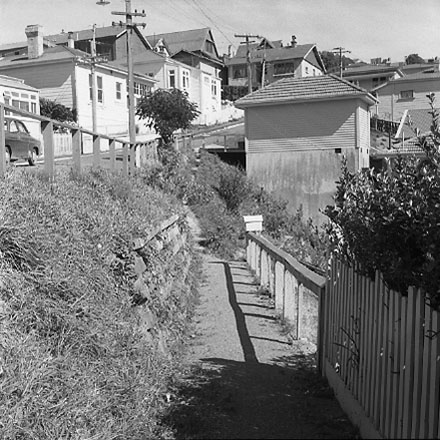 a. Views of dwelling that has been affected by a slip. Concrete retaining wall has fallen over against the house
