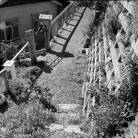 d. Views of dwelling that has been affected by a slip. Concrete retaining wall has fallen over against the house