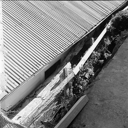 e. Views of dwelling that has been affected by a slip. Concrete retaining wall has fallen over against the house