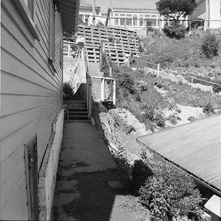 f. Views of dwelling that has been affected by a slip. Concrete retaining wall has fallen over against the house