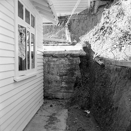 i. Views of dwelling that has been affected by a slip. Concrete retaining wall has fallen over against the house