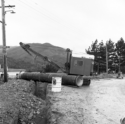 a. Views of workmen using a crane to install a new drainage pipe into trench