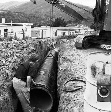 b. Views of workmen using a crane to install a new drainage pipe into trench