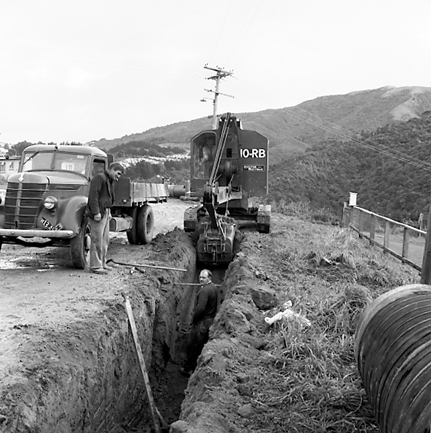 d. Views of workmen using a crane to install a new drainage pipe into trench