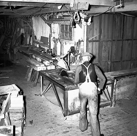 a. Interior of workshop. Workman cutting wood with a table saw