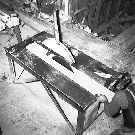 d. Interior of workshop. Workman cutting wood with a table saw