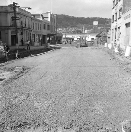 c . Views of road work being carried out by the Drainage Department. Excavation equipment and roller. In the background, W H Long &amp; Co, Foresters Arms