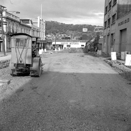 d . Views of road work being carried out by the Drainage Department. Excavation equipment and roller. In the background, W H Long &amp; Co, Foresters Arms