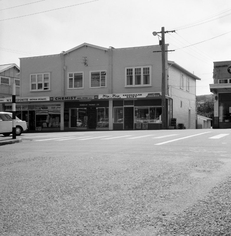 b. No. 15 Ganges Road, a two storey wooden building. Khandallah Dairy, Noel Titter Chemist and M V Goldsmith Knitwear Specialists