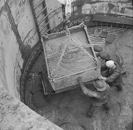 c. Views of construction, workmen using overhead crane to pour concrete