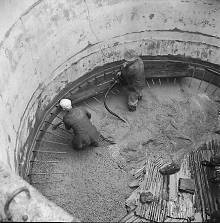e. Views of construction, workmen using overhead crane to pour concrete