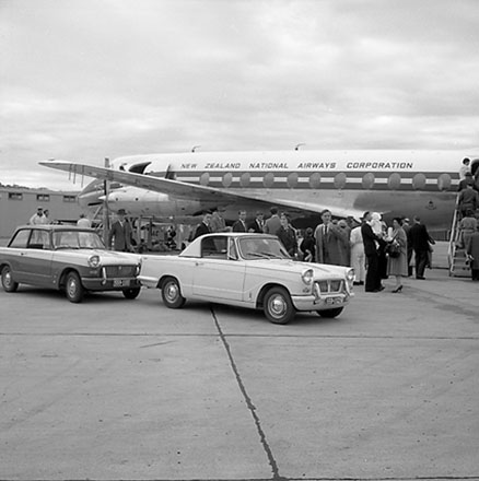 a. A Triumph motor vehicle parked in front of New Zealand National Airways Corporation aeroplane