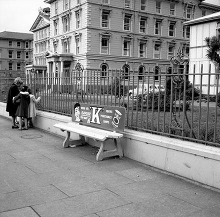 c. Wooden bus stop seat, Government Buildings, Lambton Quay, advertising for 'K' tinned fruits, vegetables and soups