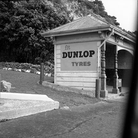 e. Unidentified location, wooden bus stop shelter, advertising for Dunlop Tyres