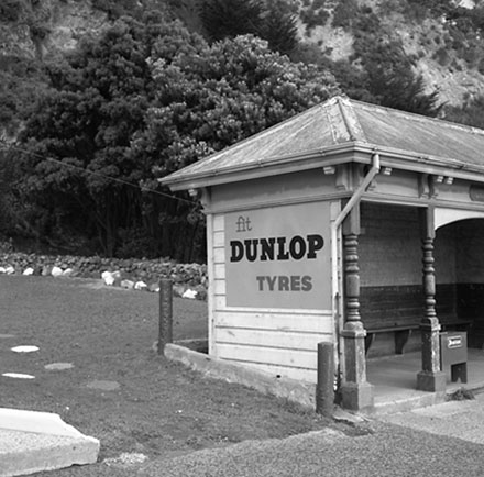 f. Unidentified location, wooden bus stop shelter, advertising for Dunlop Tyres