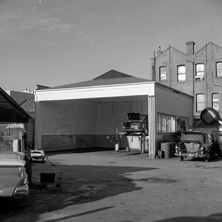 i. Unidentified location, motor garage with a vehicle up on the hoist