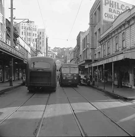 a. Two diesel buses, tramtracks and overhead wires, Roxy Theatre and Saint George Hotel in the background. Zenith Seeds Ltd on the right