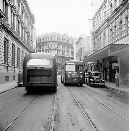 a. Two diesel buses attempting to pass. Motor Vehicles. Old Bank of New Zealand on the left, Kings Chambers in the background